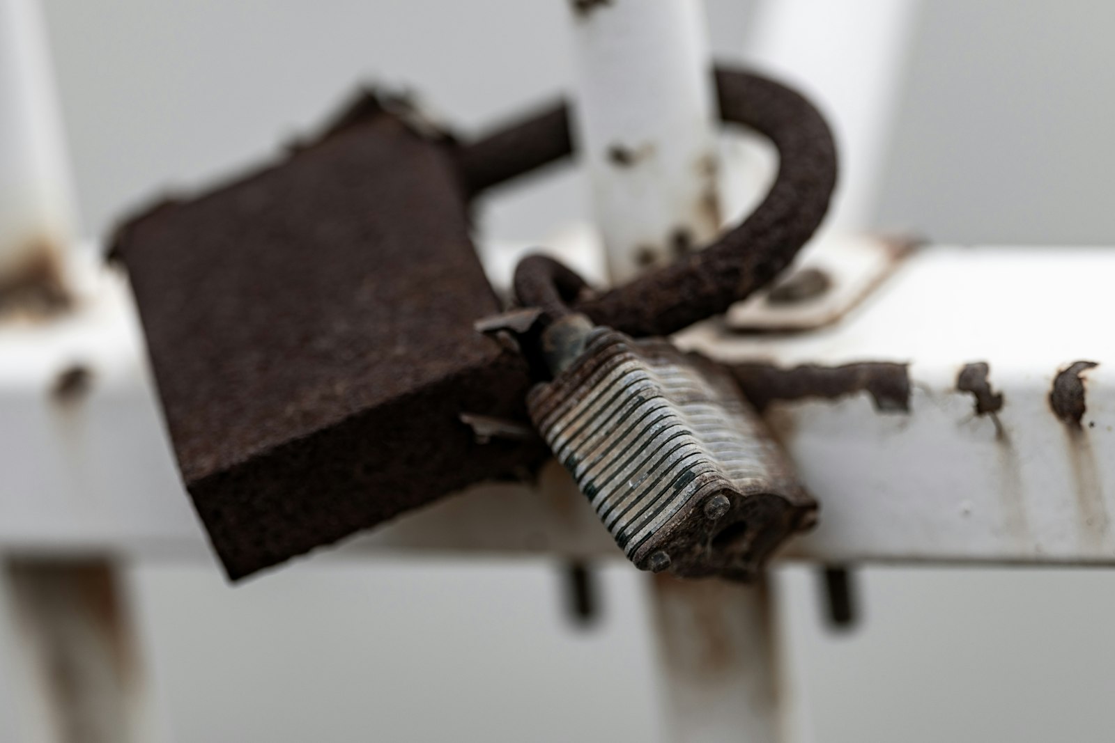 Rusted padlock hanging open on a metal rail